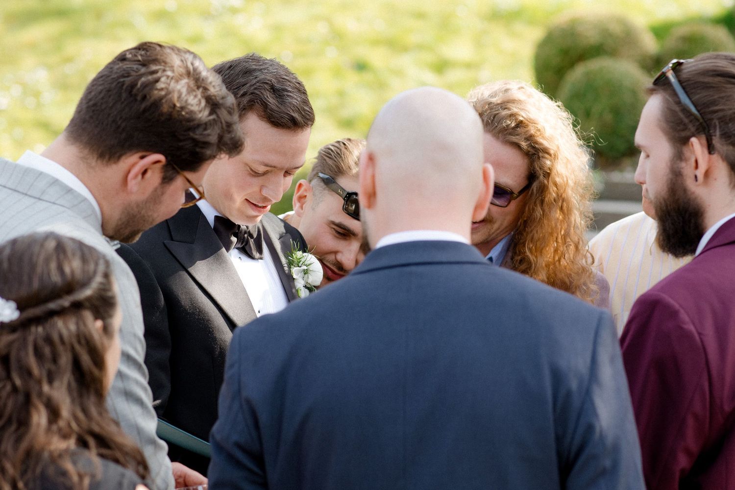 Wedding guests gathered in a circle outdoors during an intimate ceremony moment on a sunny day.