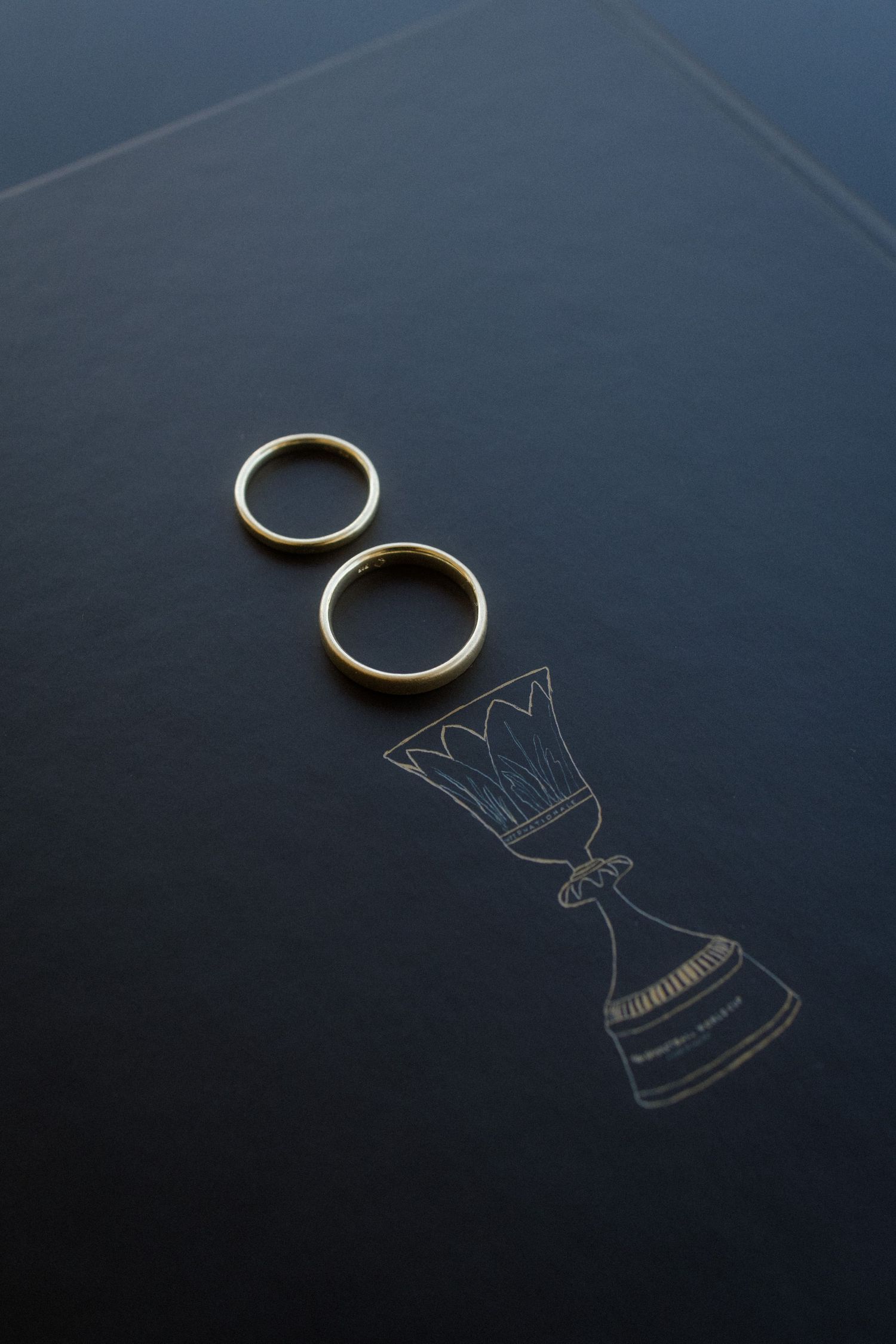 Wedding rings casting shadows creating crown silhouettes on dark blue surface.