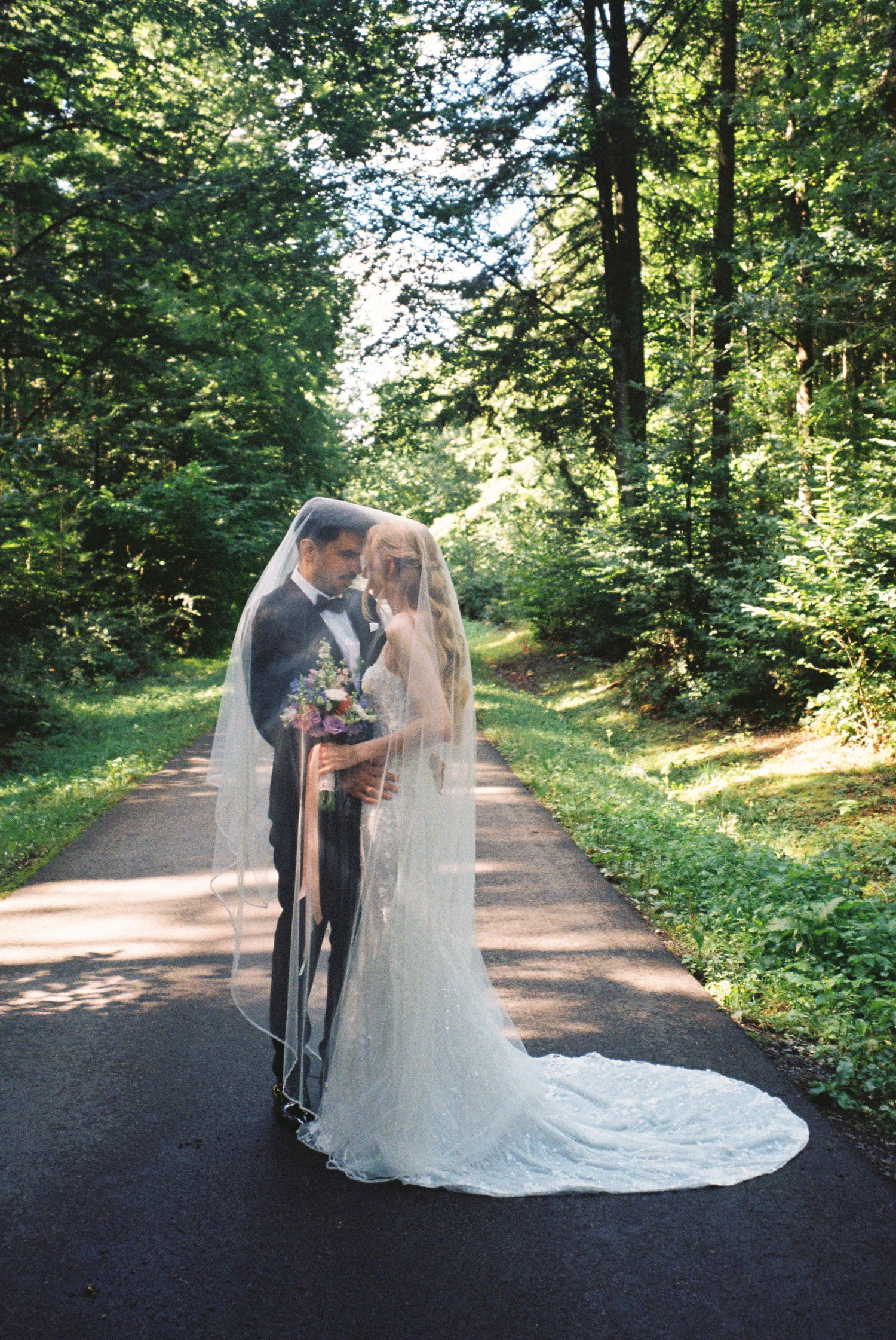 A couple shares a romantic moment on a tree-lined path during their outdoor wedding photoshoot.