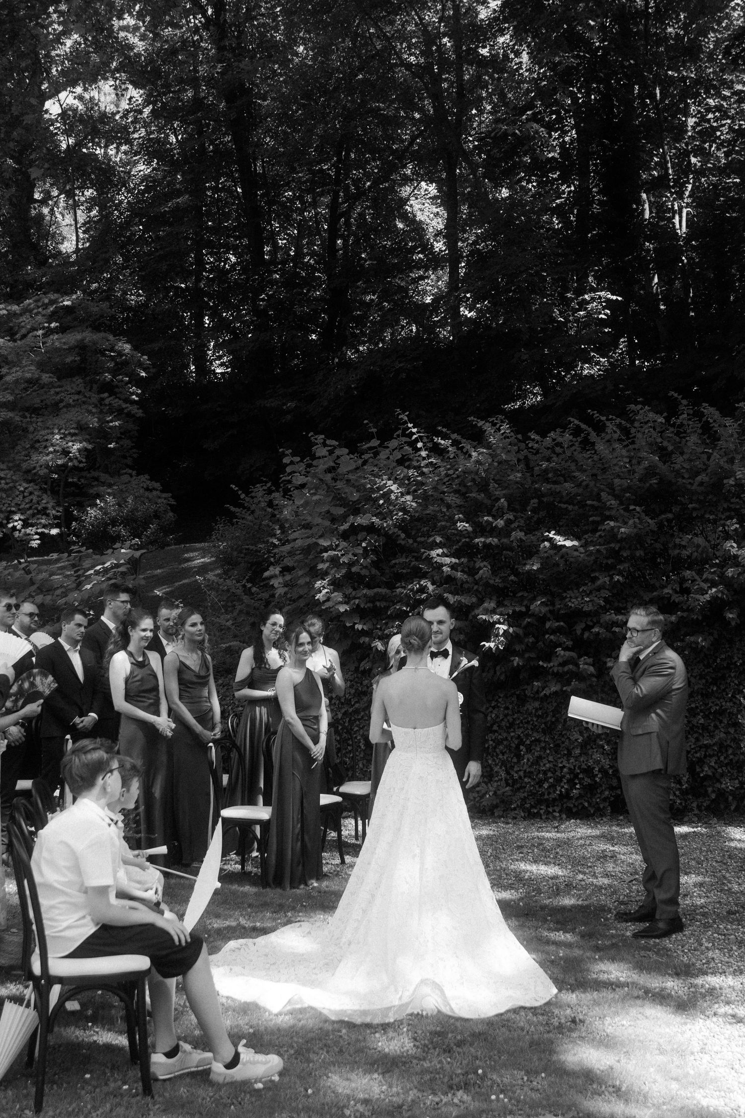 Outdoor wedding ceremony in lush garden with bride in white gown facing groom at the altar.