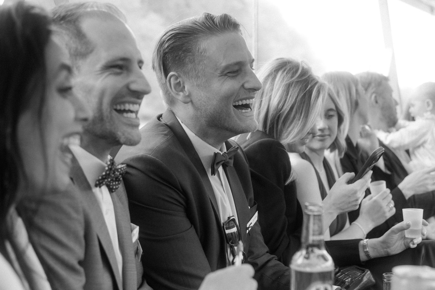 Black and white photo of laughing wedding guests seated together at reception table.