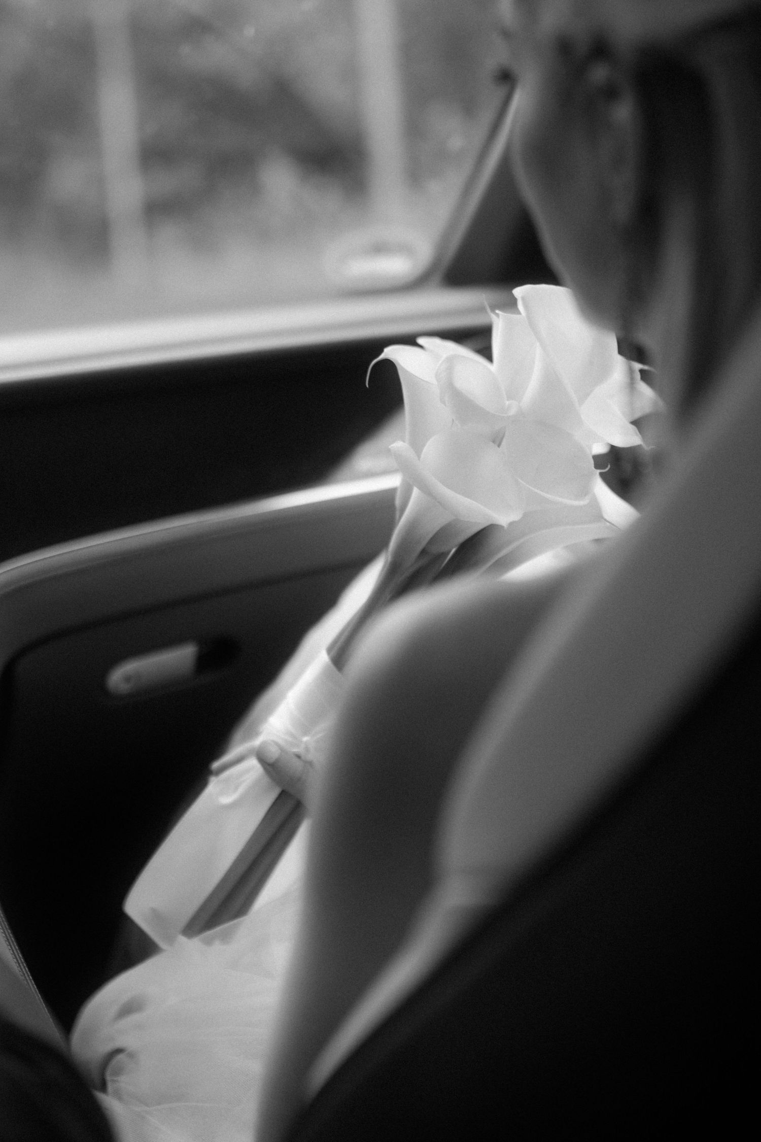 A white lily flower rests on a car seat, captured in black and white with soft focus.