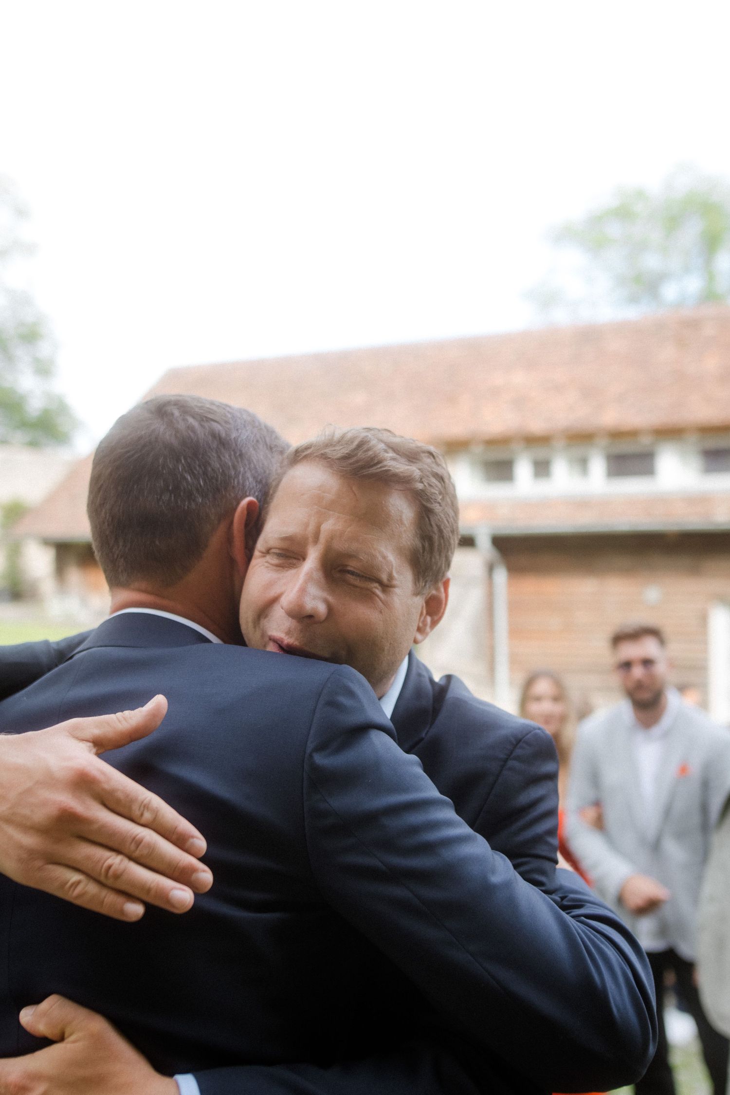 Emotional embrace between wedding guests during outdoor celebration.