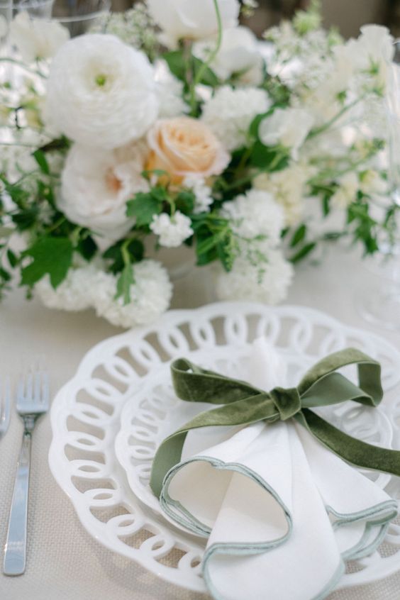 White and peach floral arrangement with a green ribbon on a lace-trimmed plate setting.