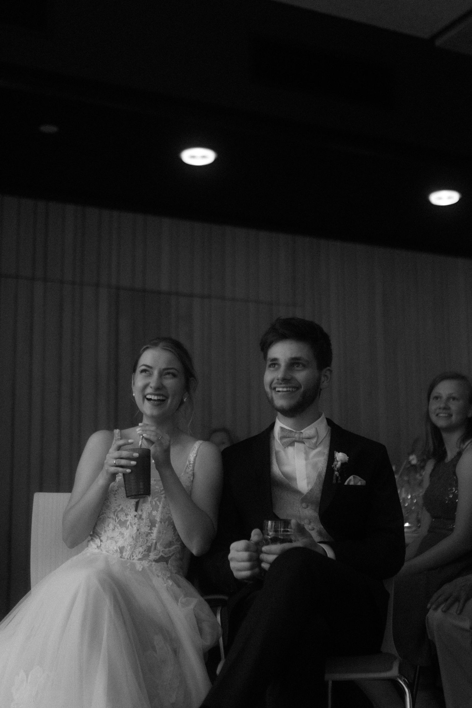A candid black and white photo of wedding reception guests enjoying drinks and laughter.