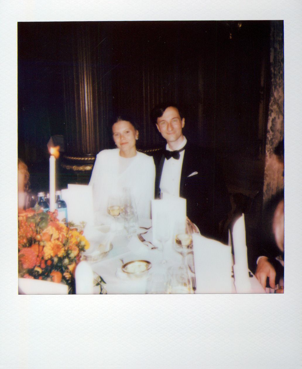 Guests seated at an elegant dinner table with white tablecloths and formal place settings.