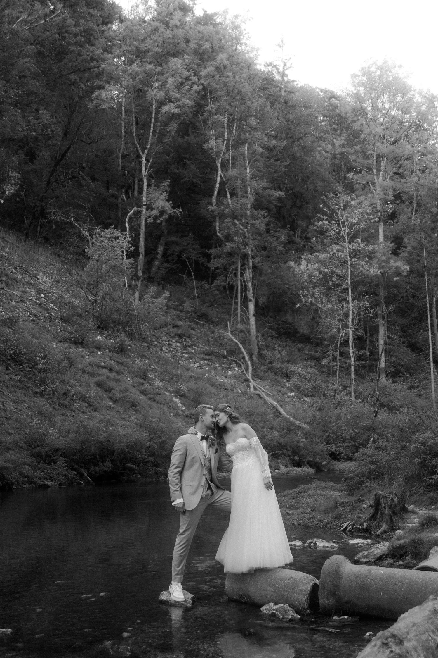 Black and white photo of couple by scenic woodland lake.