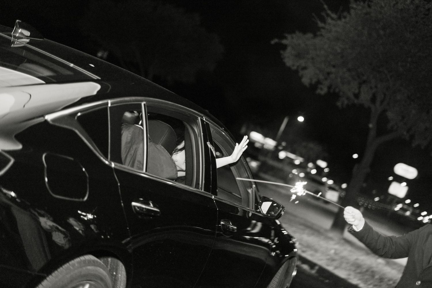 A black vintage car photographed at night with streetlights creating a moody atmosphere in black and white.