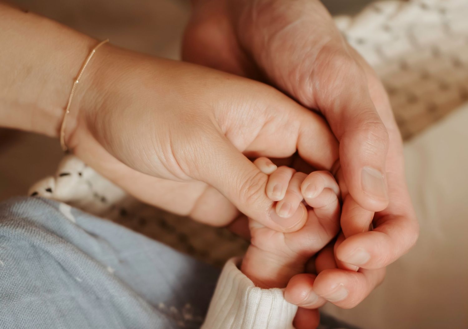 A tender moment captured as a tiny baby's hand grasps an adult finger against a soft blurred background.