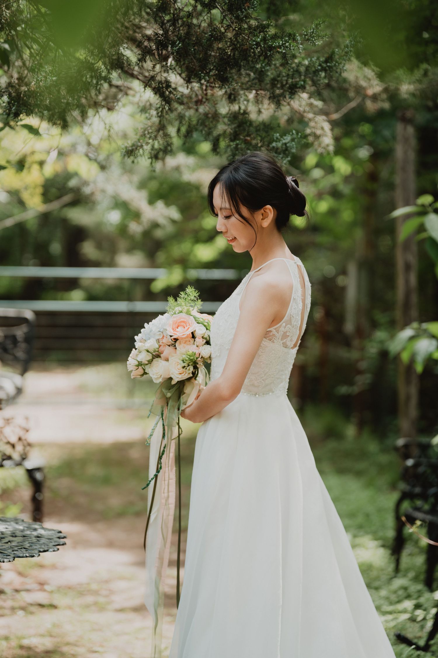 A bride in a white lace dress holds a pink and white floral bouquet in a garden setting.