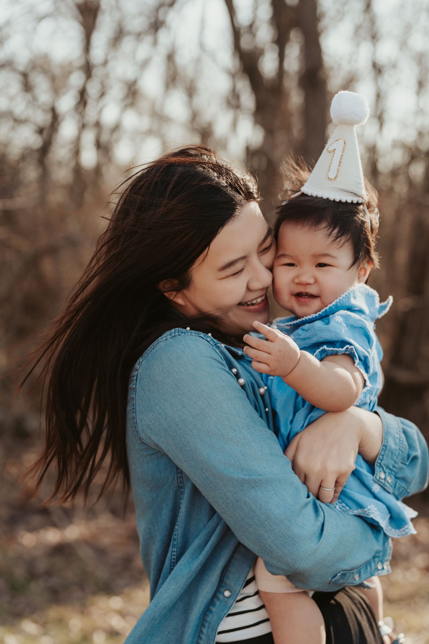 A joyful outdoor family moment captured between parent and child wearing matching blue outfits and a party hat.
