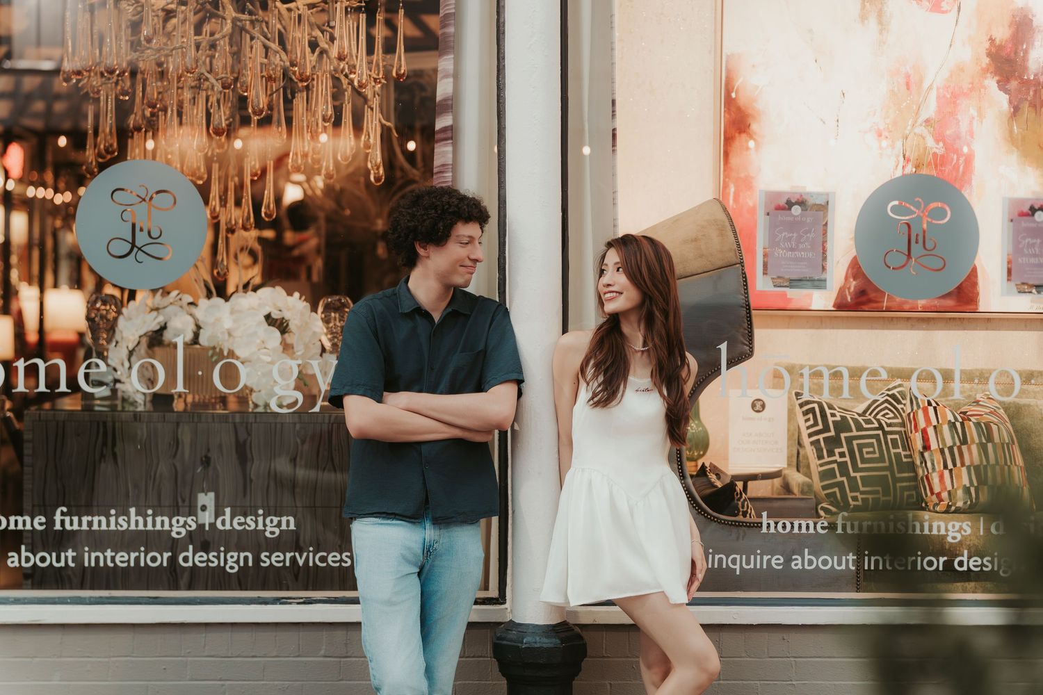 A couple shares a sweet moment outside a storefront with blue decor and hanging lights at dusk.