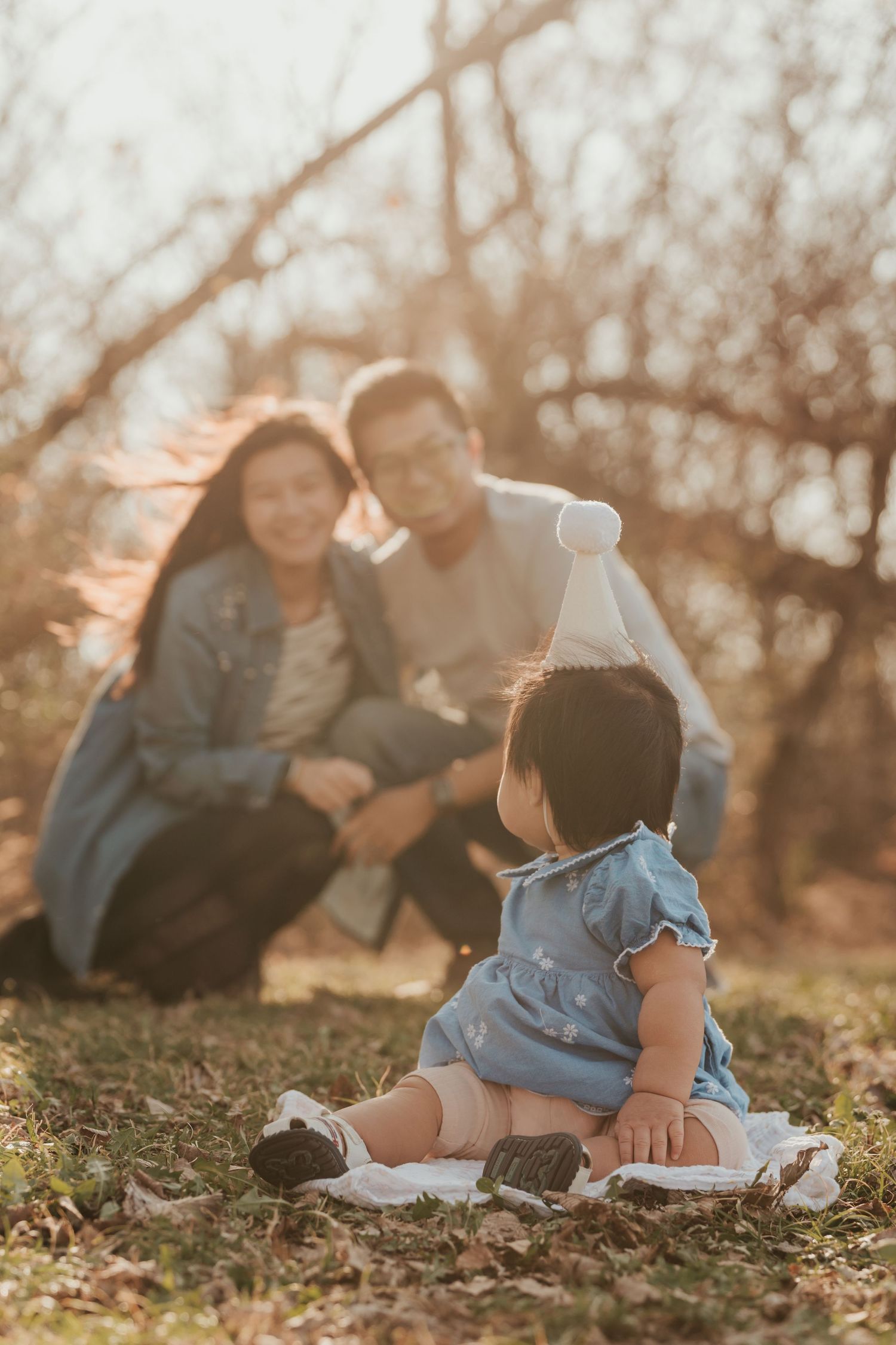 A family sits together on autumn ground during golden hour sunset in a heartwarming outdoor portrait session.