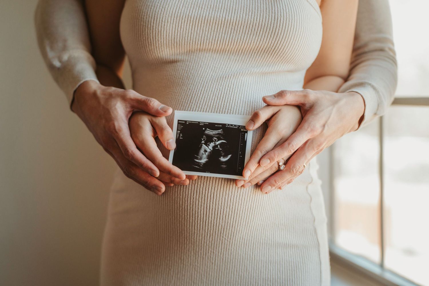 Someone in a cream sweater dress holds a black and white sonogram photo showing a baby's ultrasound image.