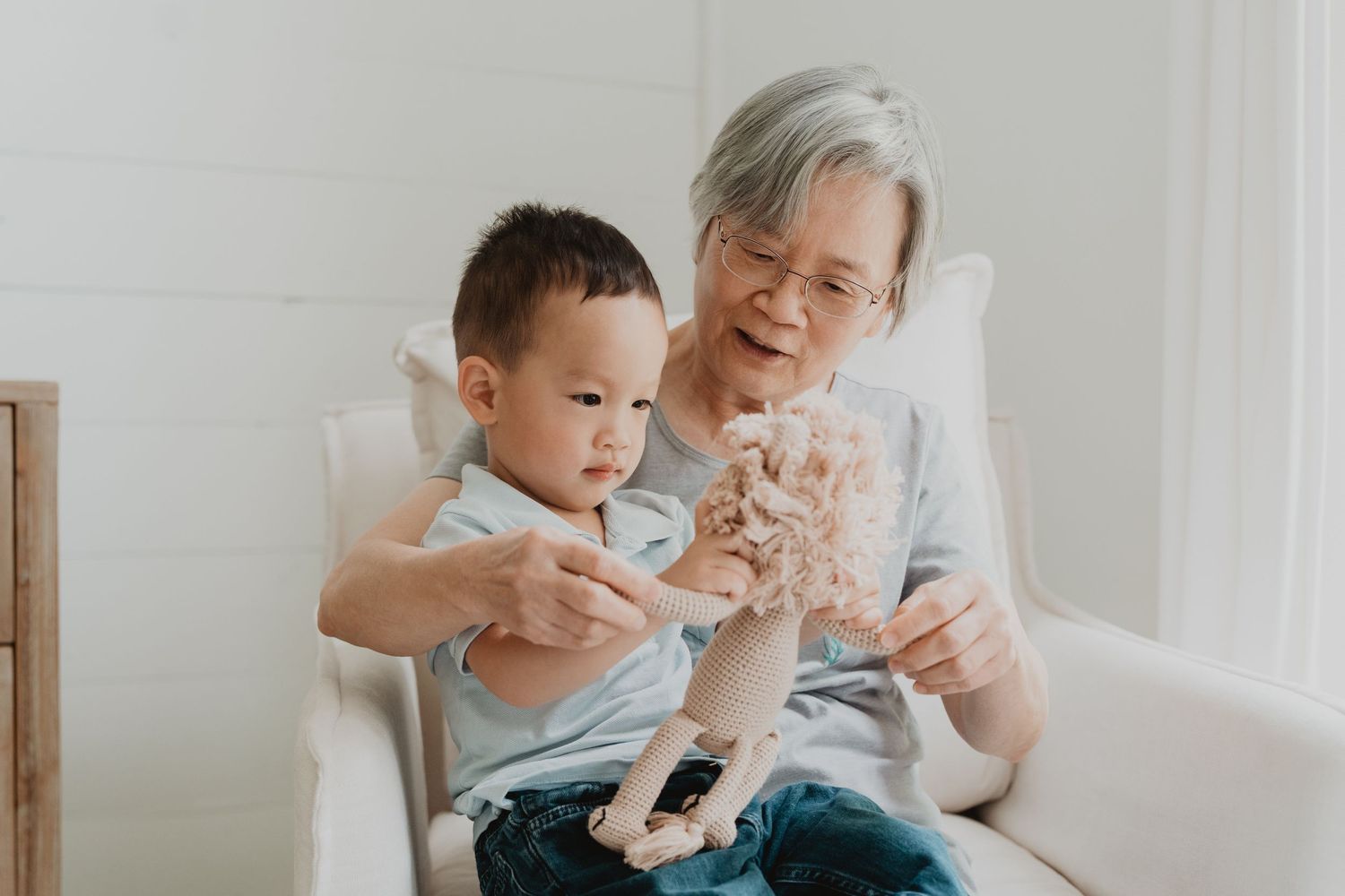 Two people sit together on a couch playing with a small toy animal in a bright, minimalist room.