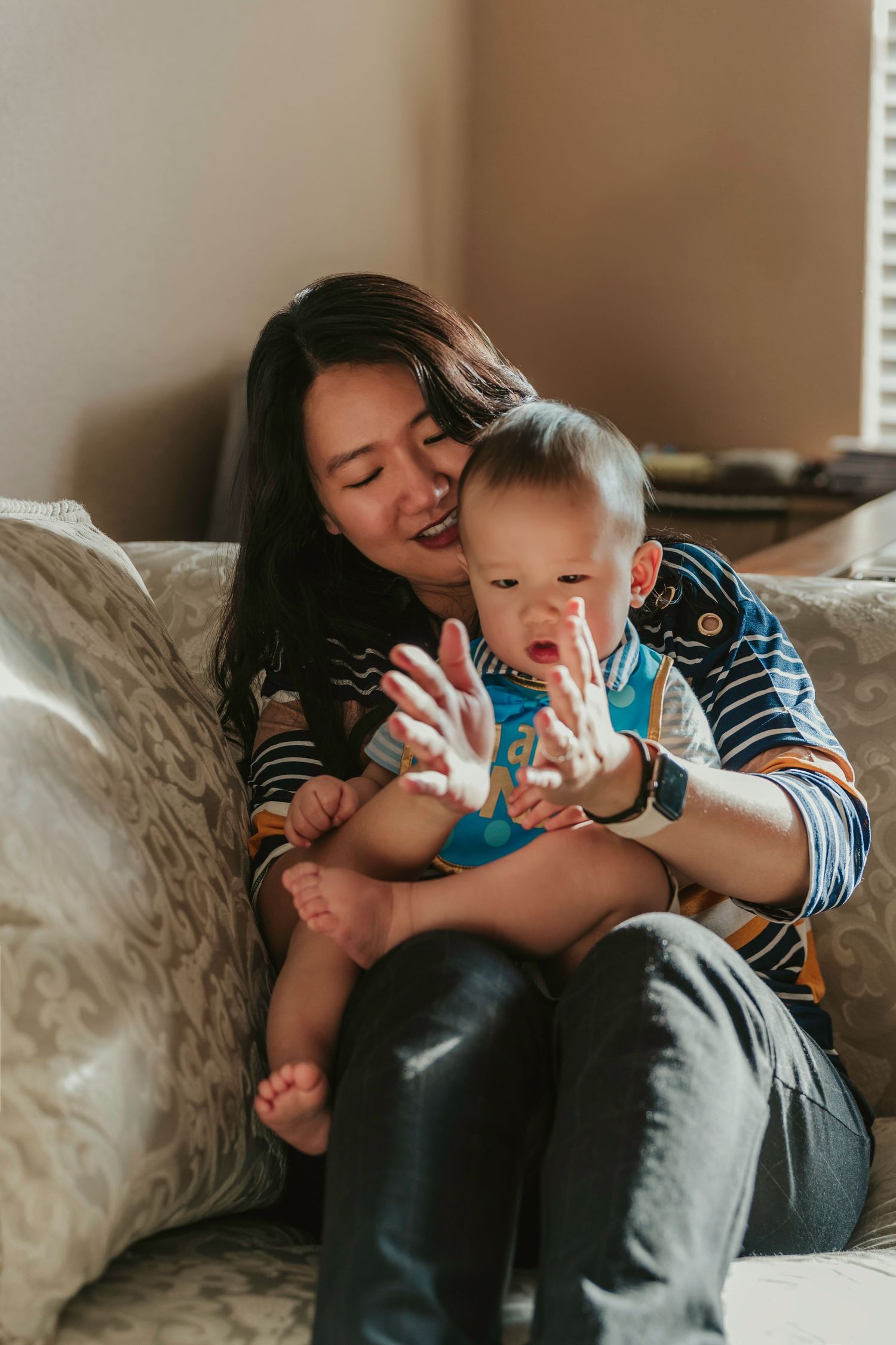 A tender moment between a caregiver and baby sitting together on a cozy beige couch in warm natural lighting.