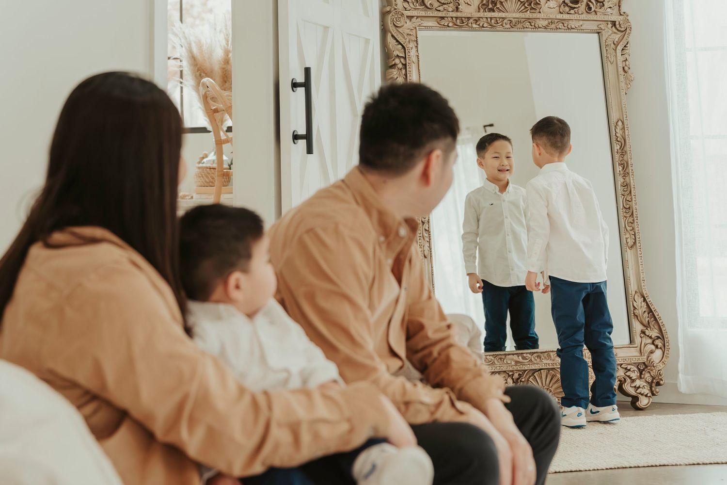 A family sitting together by a large ornate mirror, creating a warm and intimate indoor portrait scene.