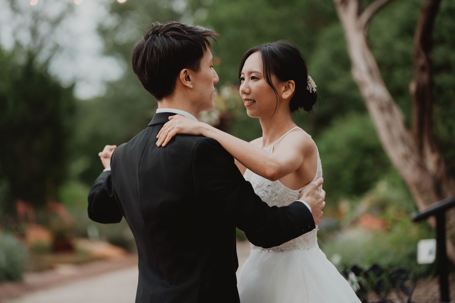 A romantic couple embraces while dancing in a garden pathway on their wedding day.