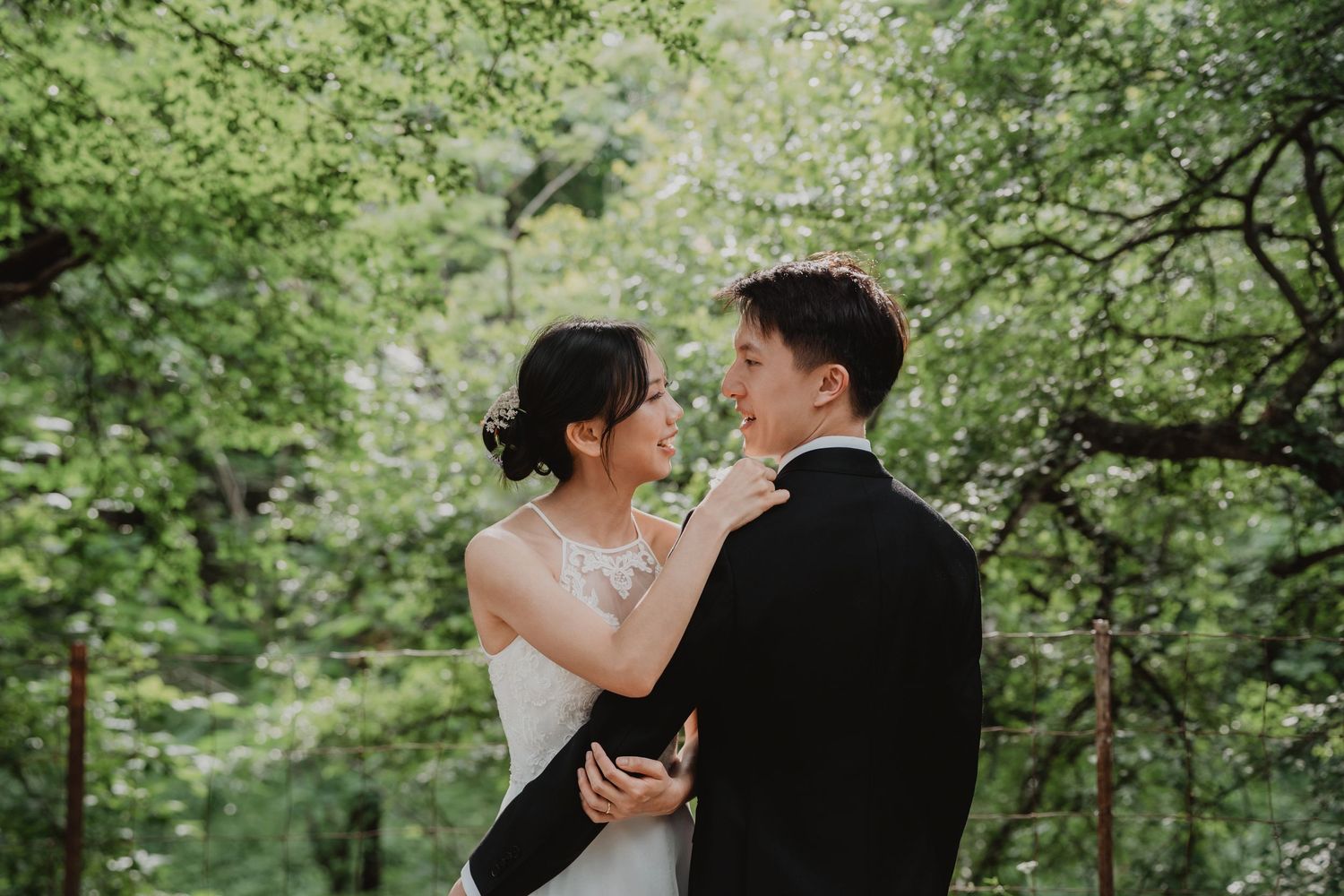 A couple in wedding attire share a romantic moment surrounded by lush green forest scenery.