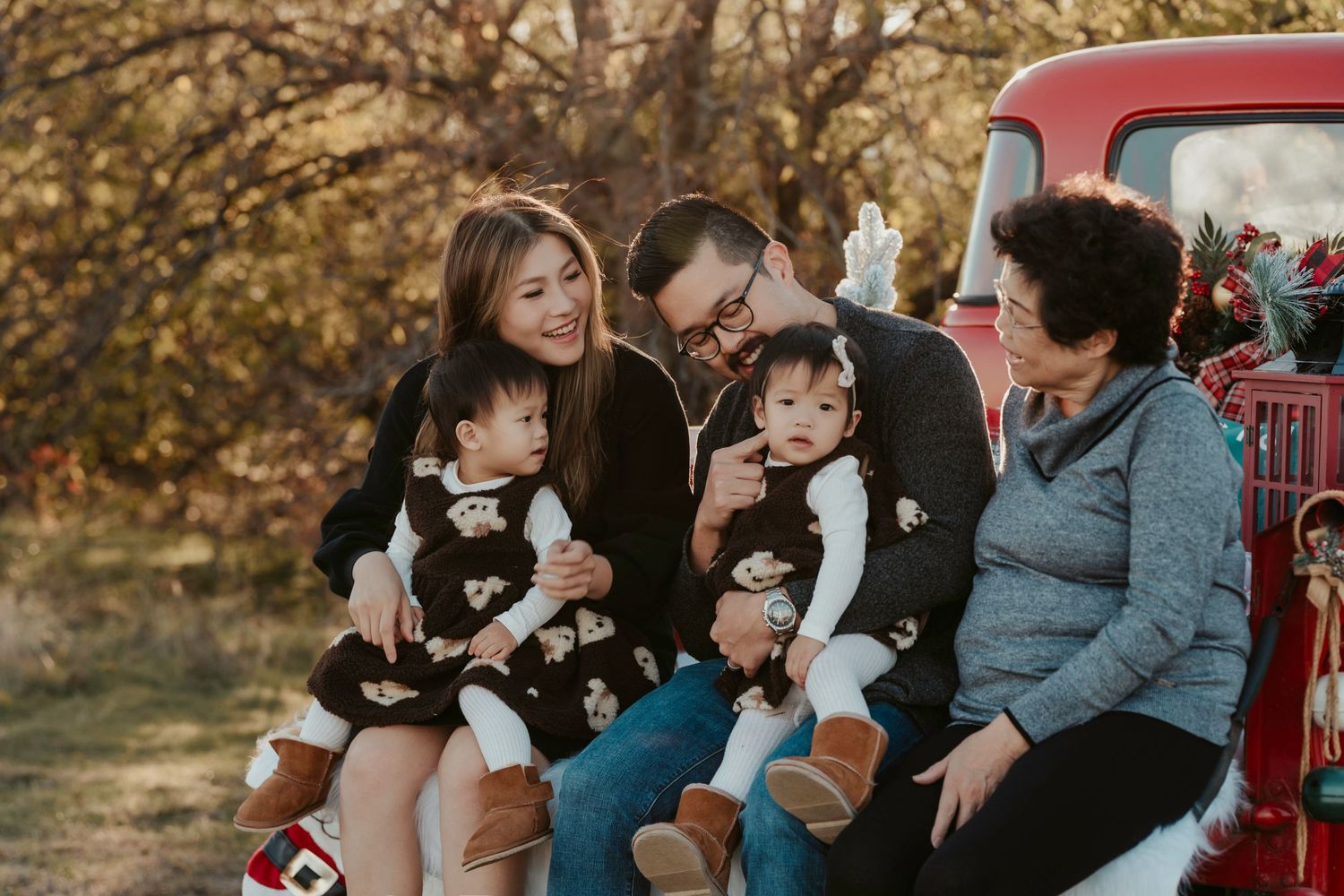 Family sitting together on vintage red pickup truck during autumn photoshoot in warm evening light.