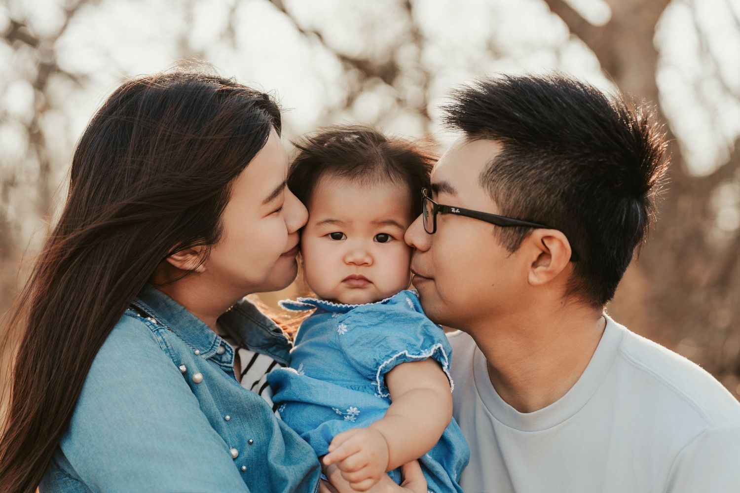 A happy young family shares tender moments together while wearing matching blue outfits in an outdoor setting.