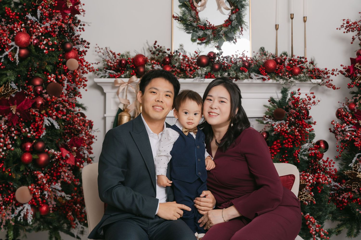 Family poses together for holiday photos in front of festive red and green Christmas decorations and wreaths.