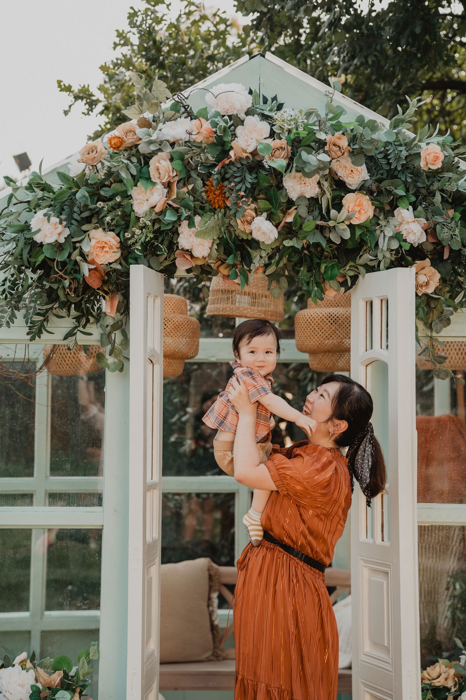Rustic outdoor scene with French doors decorated with peach and orange roses and greenery under a garden arbor.