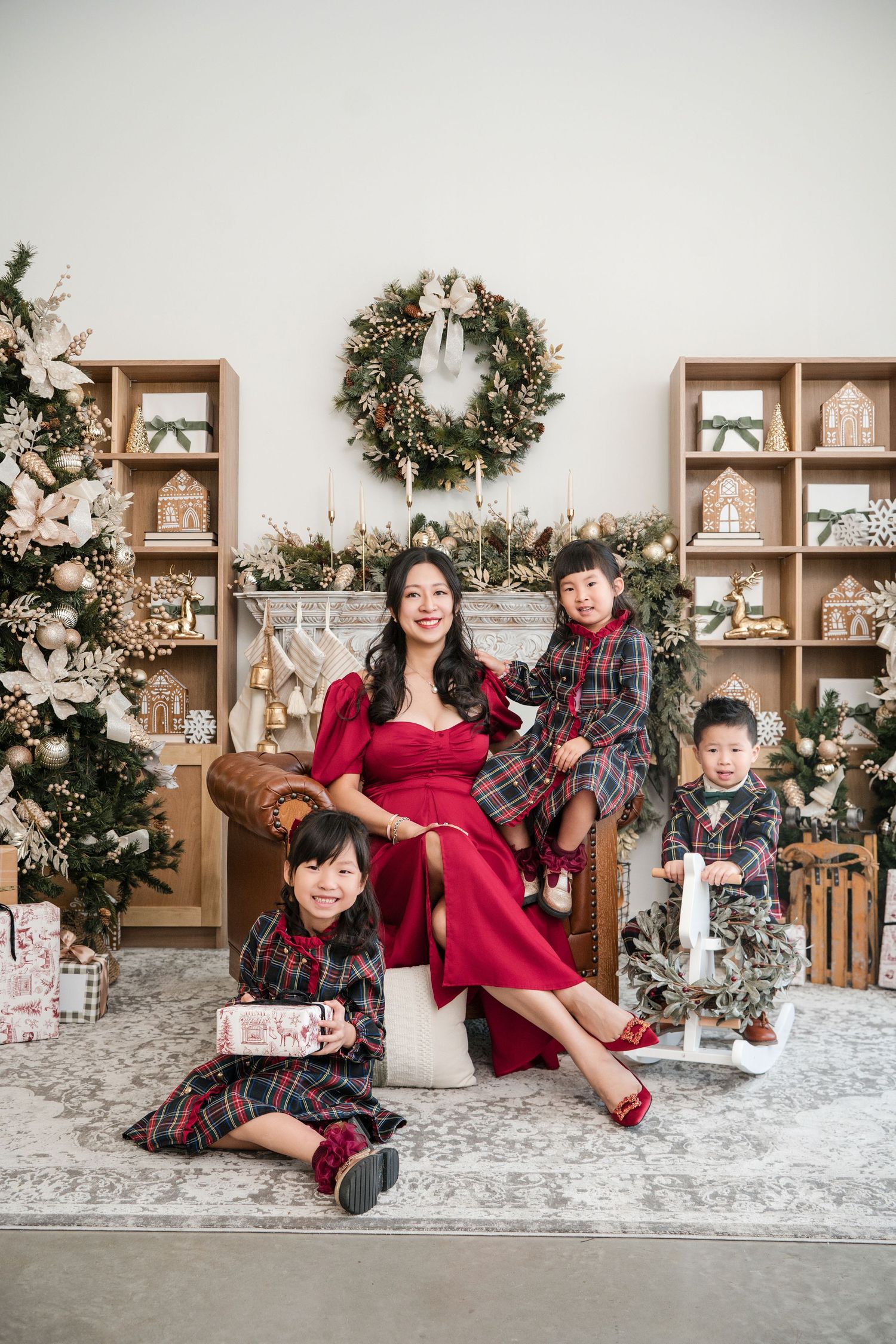 Holiday family portrait with festive decor featuring matching plaid outfits, wooden shelves and Christmas wreath.