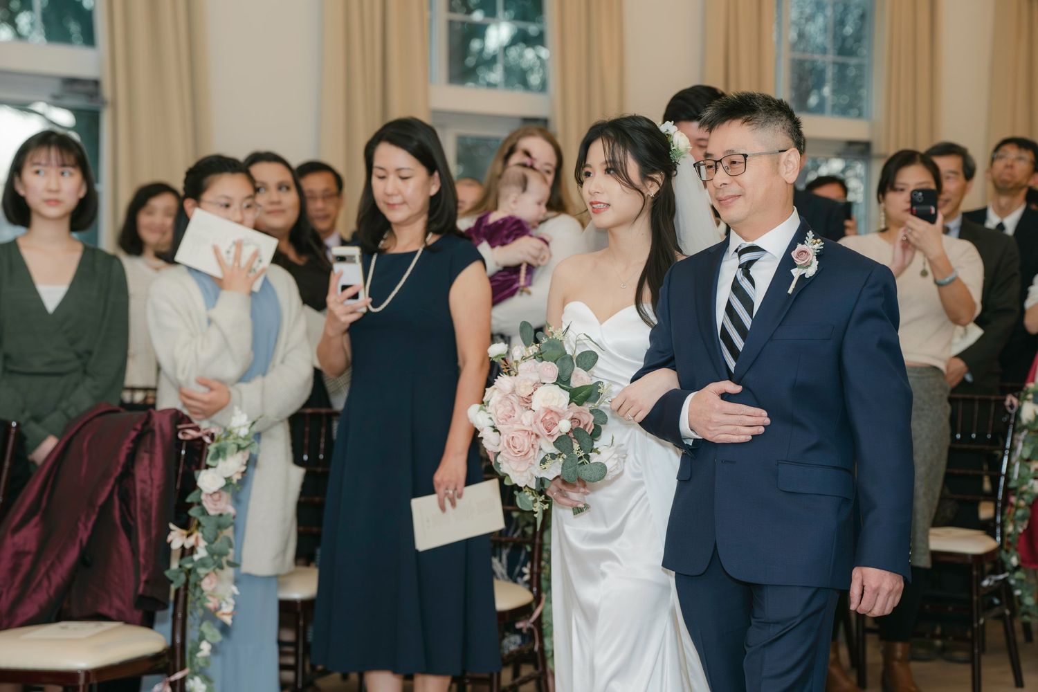 A wedding ceremony takes place indoors with guests gathered to celebrate as the couple stands at the front.