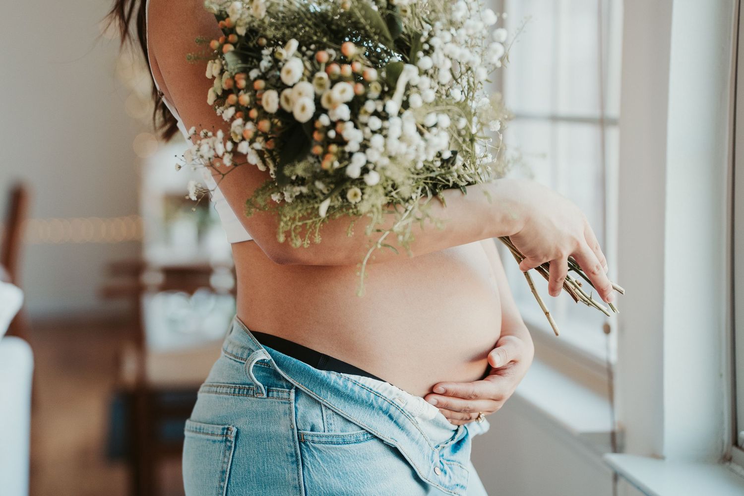 Close up view of a pregnant belly with delicate baby's breath flowers and light pink top and jeans.