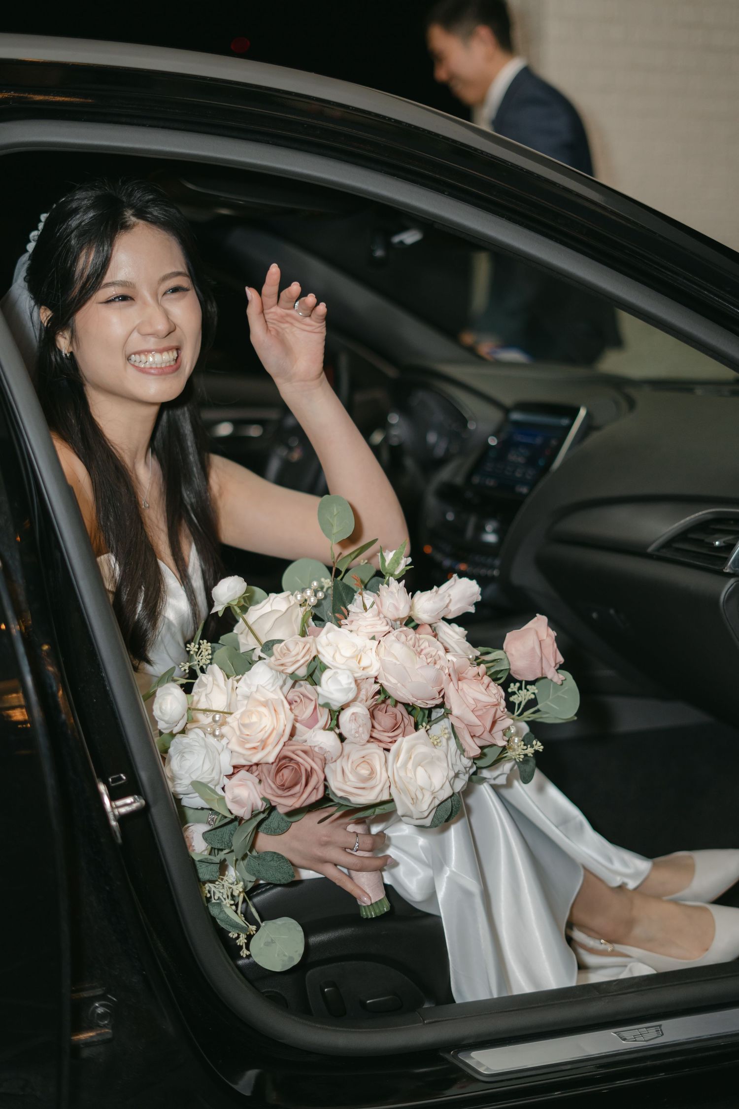 An elegant bouquet of pink and white roses sits in a car with a wedding dress visible.