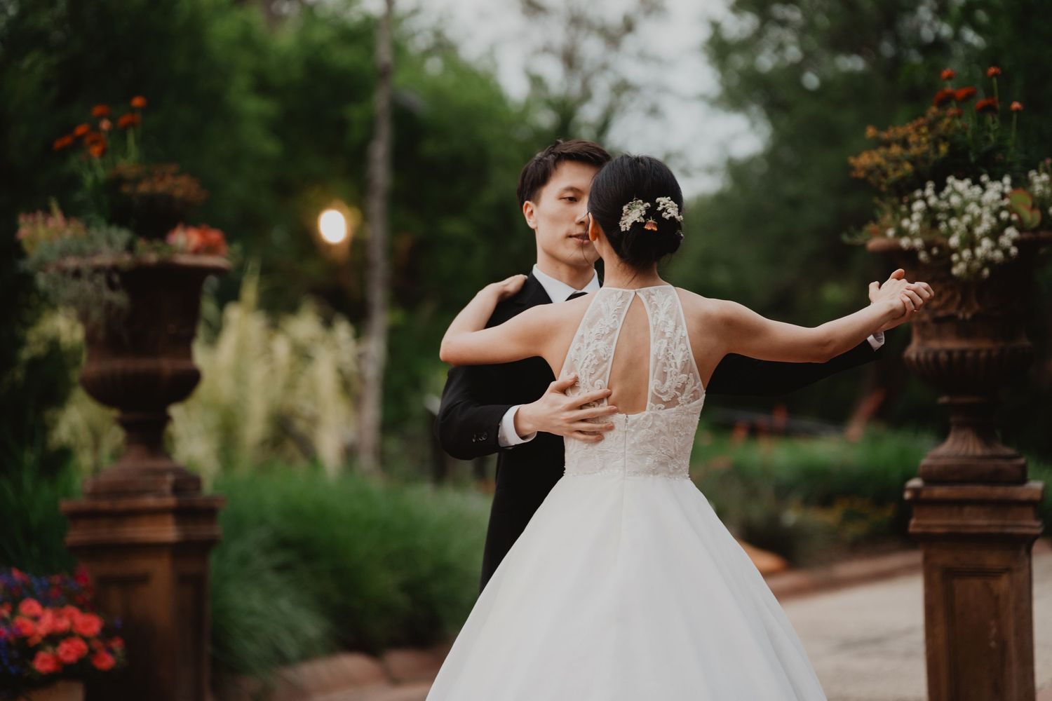 A couple dances gracefully in a garden setting at dusk, with the bride wearing a classic white ball gown.
