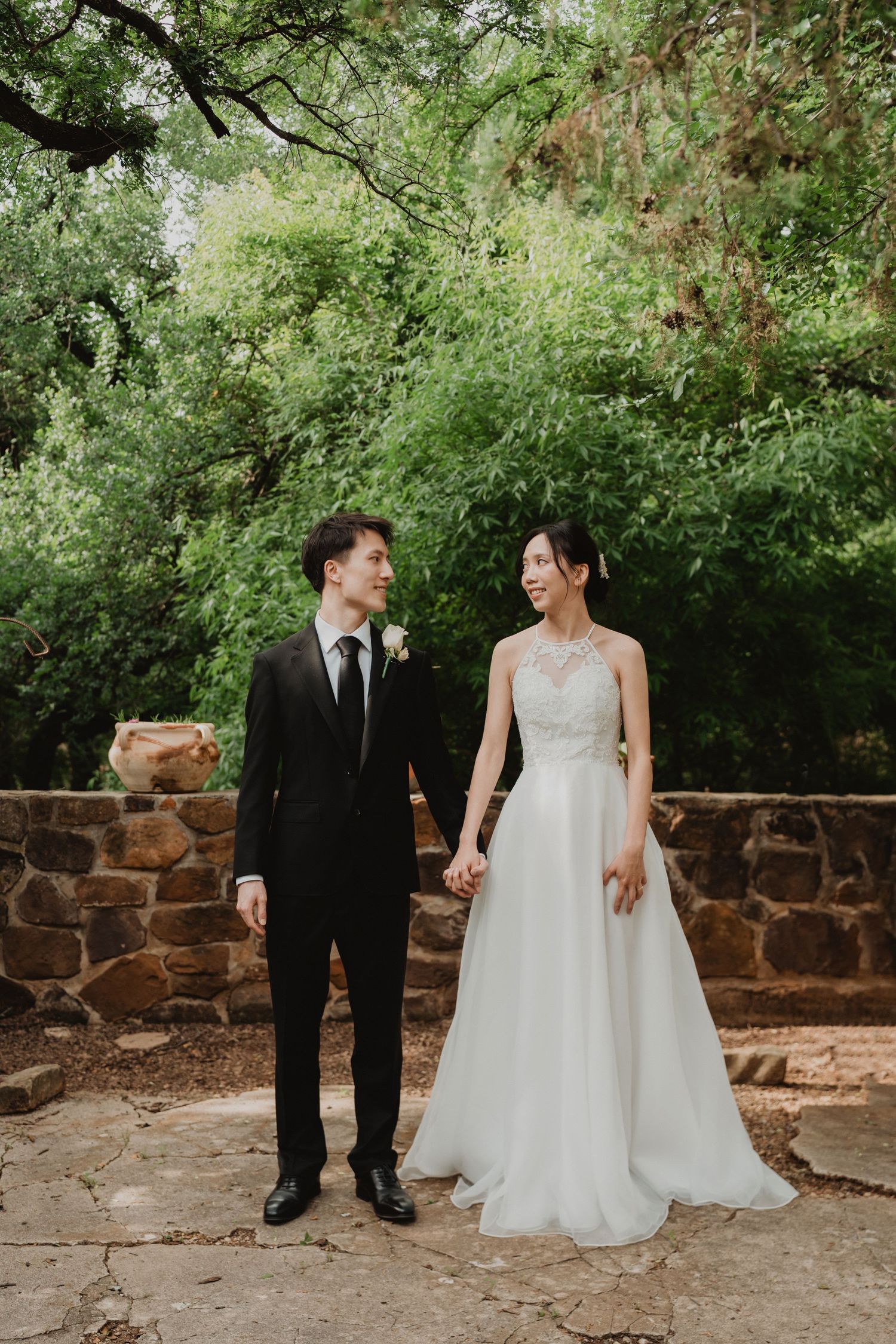 A wedding couple shares a joyful moment surrounded by lush greenery and stone walls in a romantic outdoor setting.