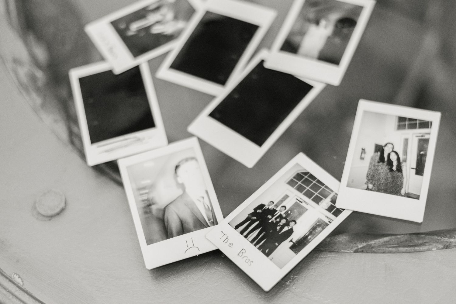 A collection of vintage polaroid photographs scattered on a light surface shown in black and white.