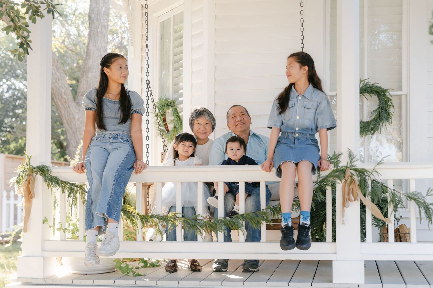 A group of people sitting and posing casually on a white porch railing in denim outfits.