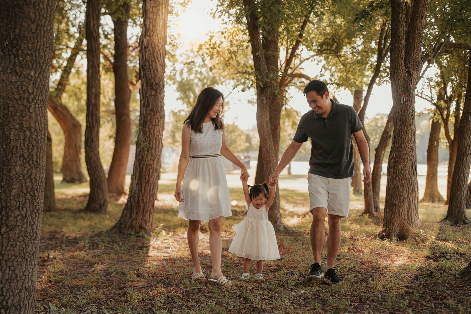 A family holds hands while walking through a sunlit forest path on a warm autumn afternoon.