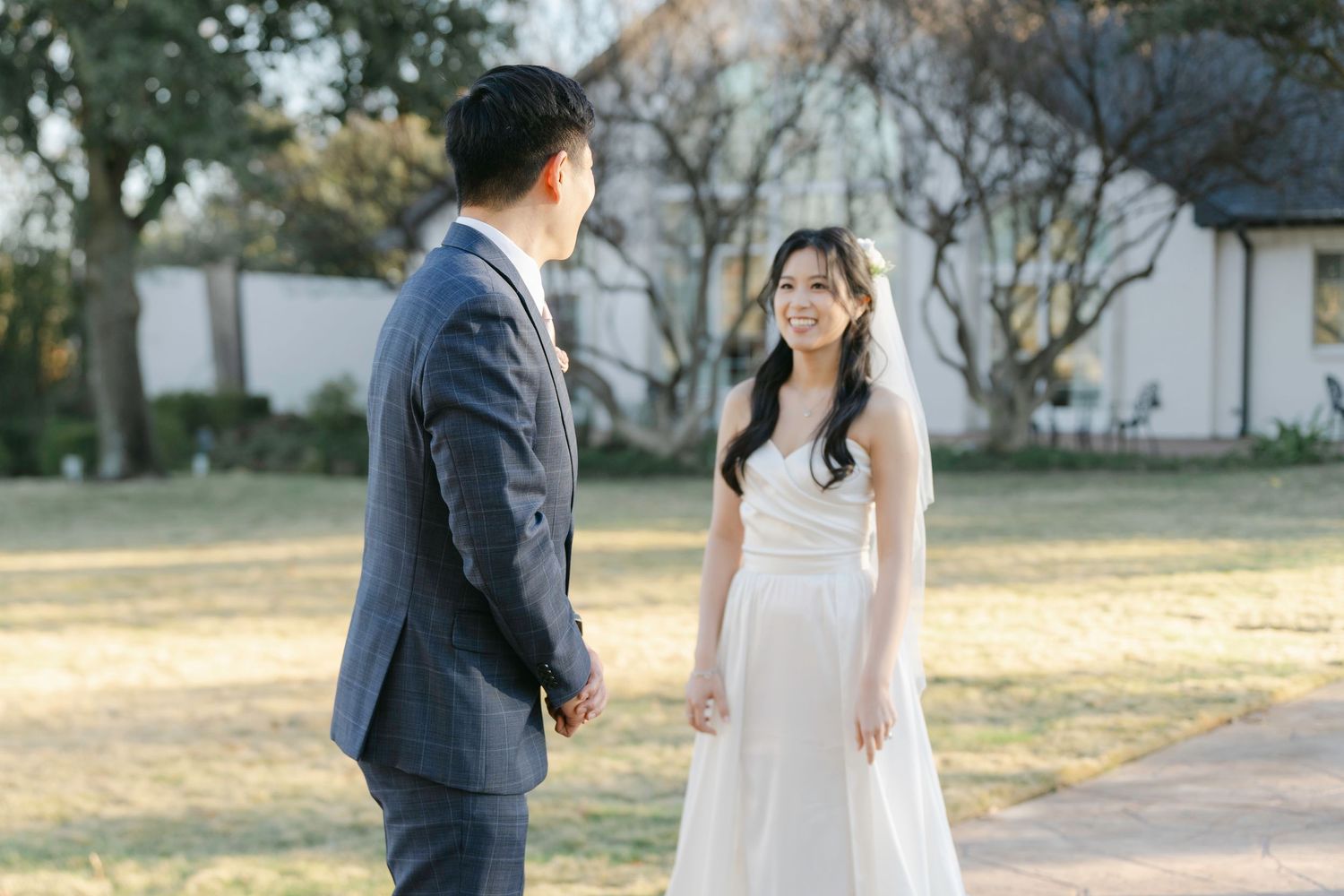 A romantic outdoor wedding scene shows couple in elegant attire standing on a garden path surrounded by trees.