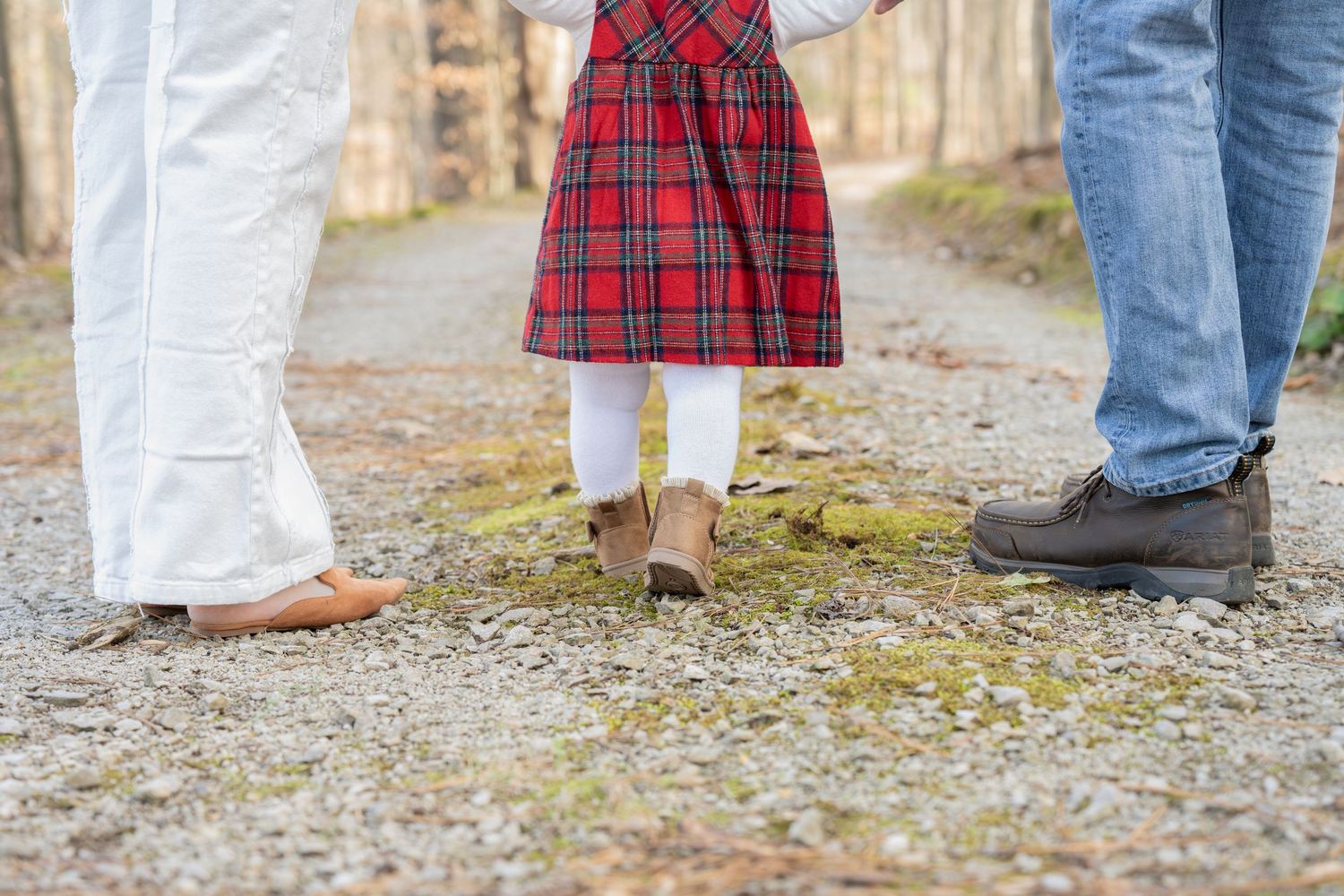 Family members wearing coordinated red plaid and white outfits stand together on a gravel path during a holiday photo shoot.
