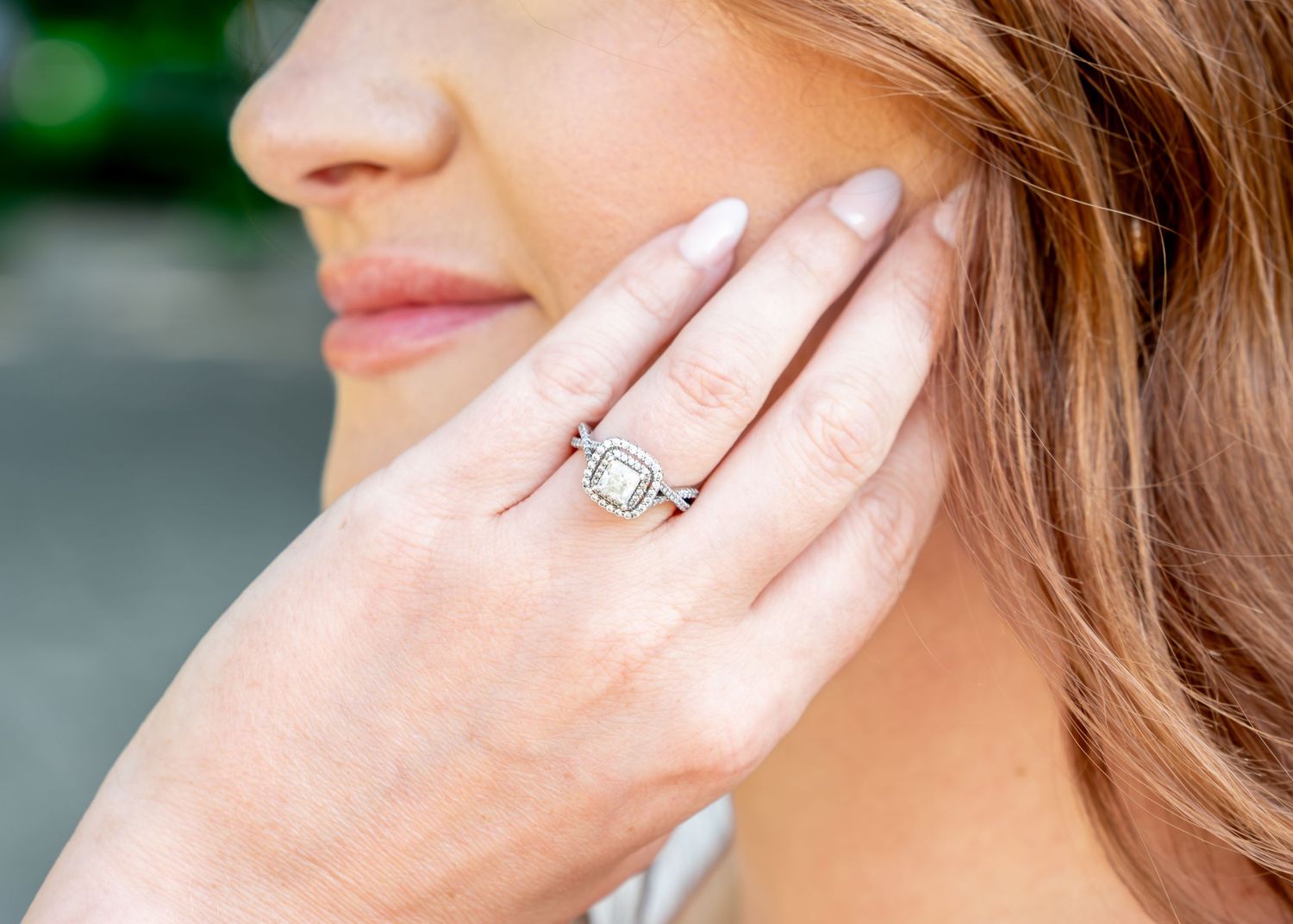 Close-up of hand wearing elegant emerald cut diamond engagement ring with pave band against blurred background.