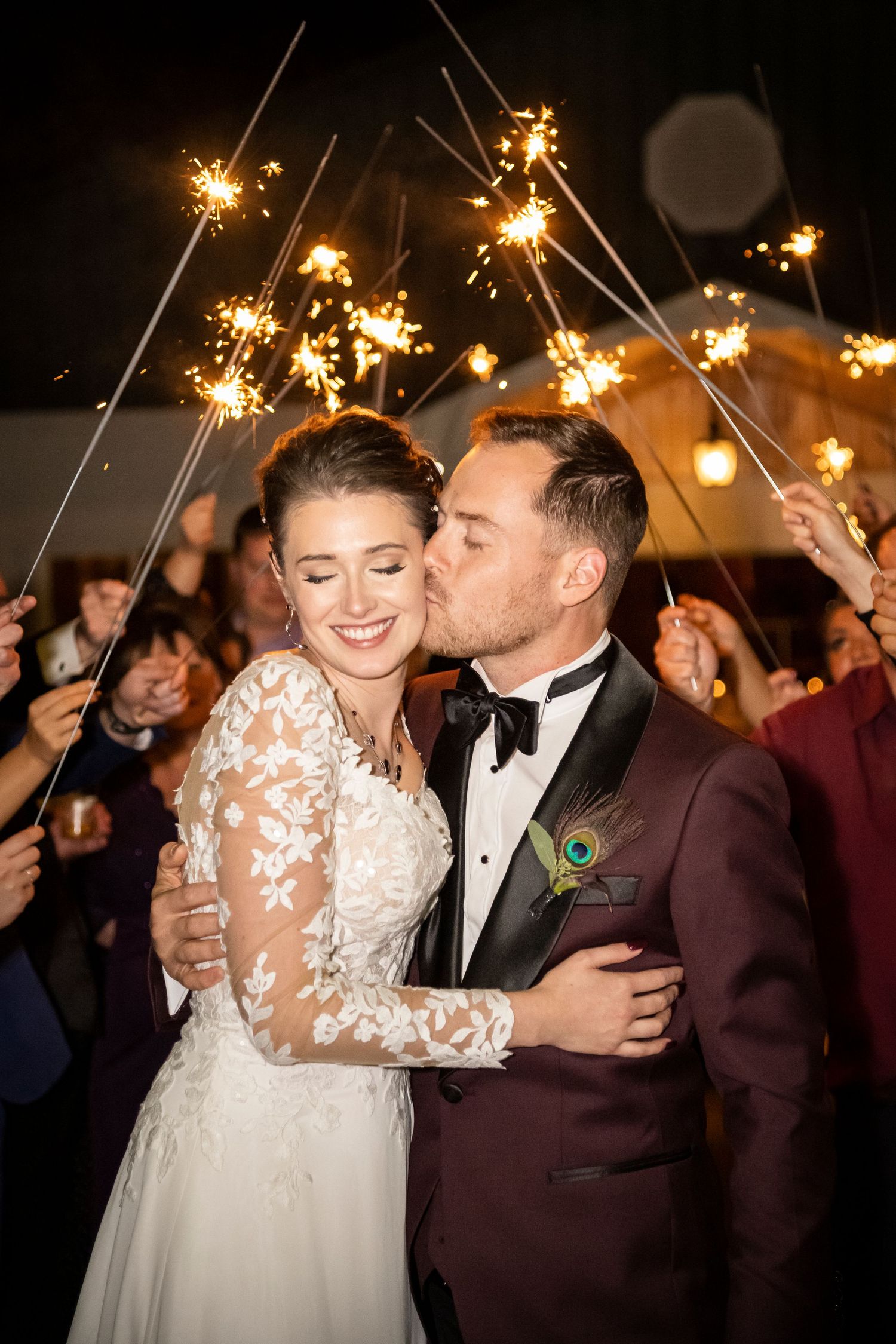 Sparkler exit showcases bride and groom in embrace as the groom kisses his bride on the cheek.