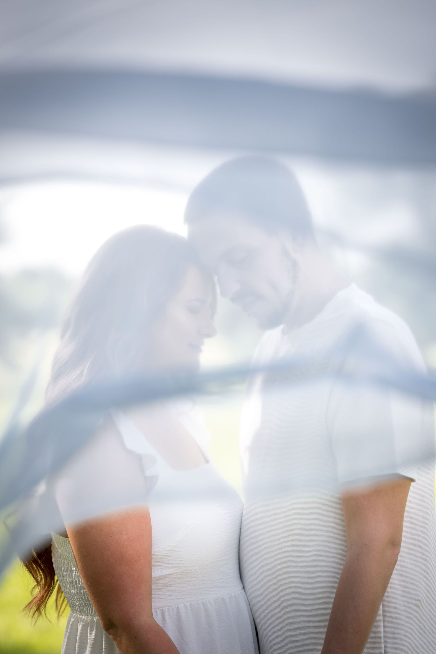 A romantic ethereal portrait of a couple in white clothing standing close together in soft dreamy lighting.