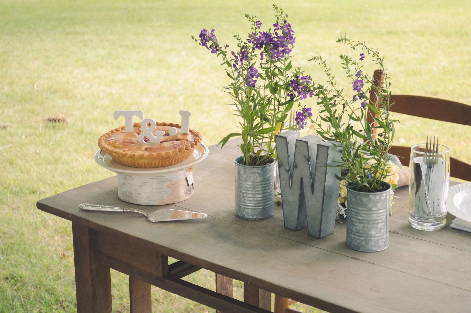 Rustic wooden table outdoors with decorative Mason jars filled with purple wildflowers and antique home decor pieces.