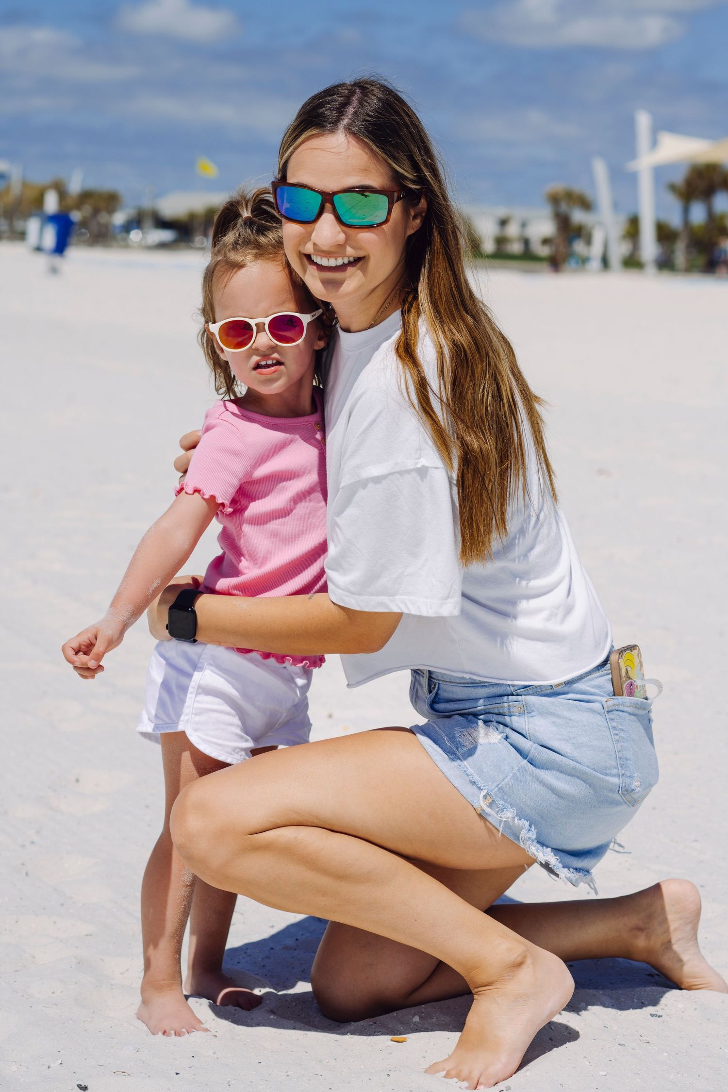Two people wearing colorful sunglasses enjoy a sunny day together on a white sandy beach.