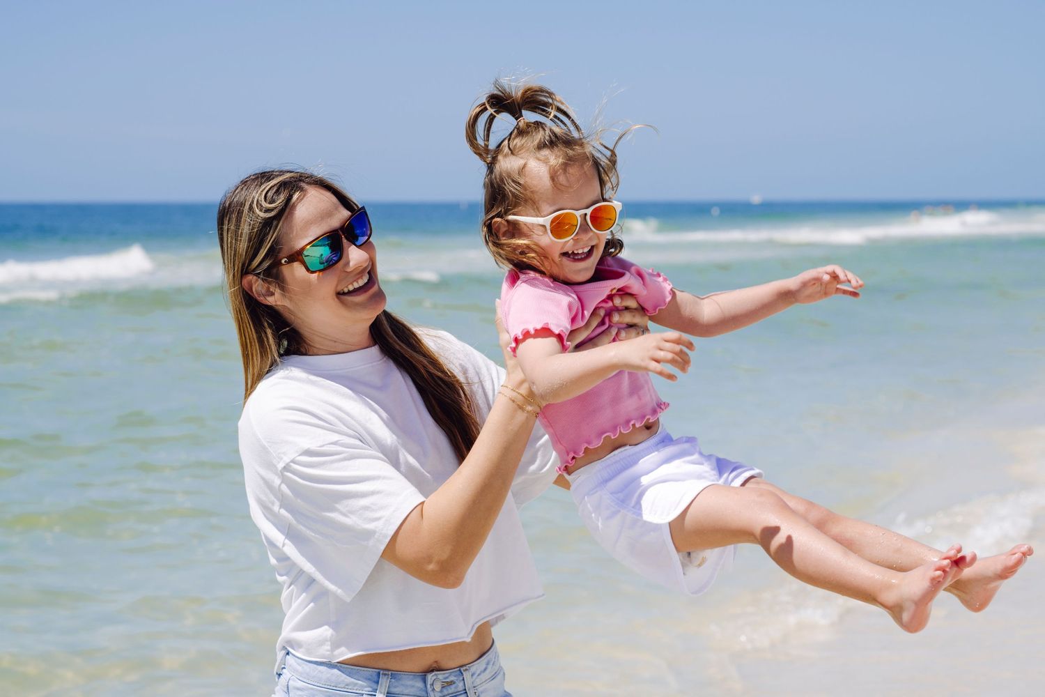 Two people enjoying a playful moment at the beach on a sunny day with blue ocean waves in the background.