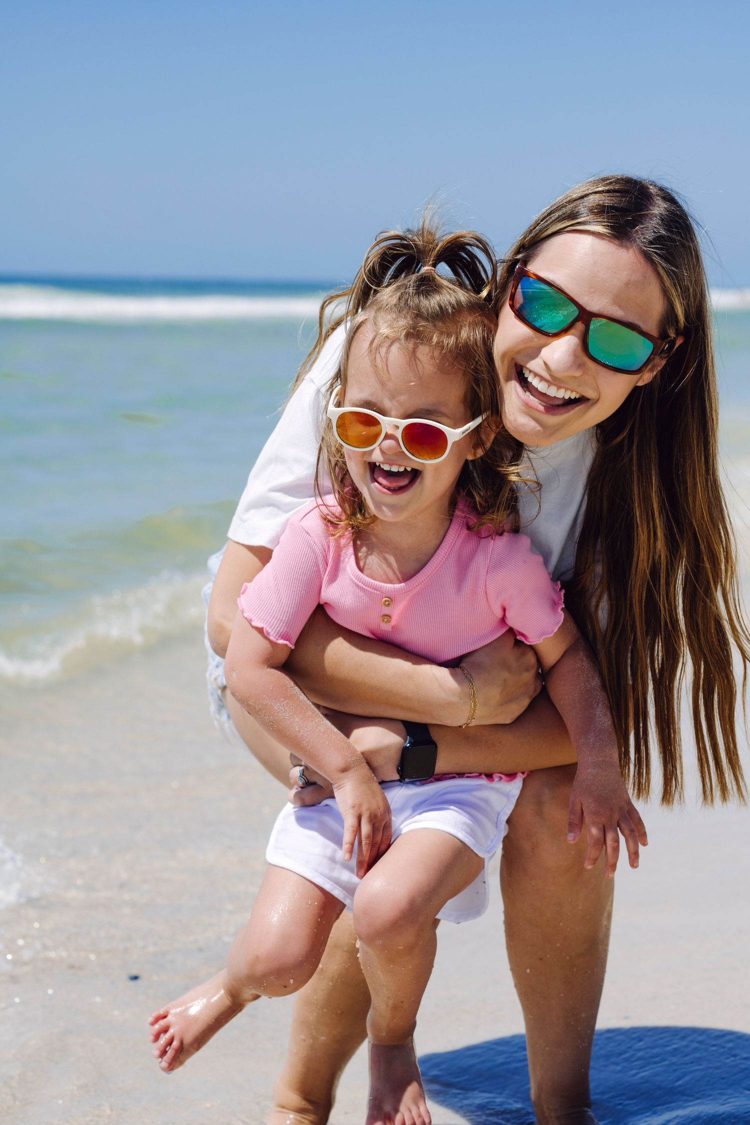 People in sunglasses having fun together at sunny beach with rolling waves and blue ocean in background.