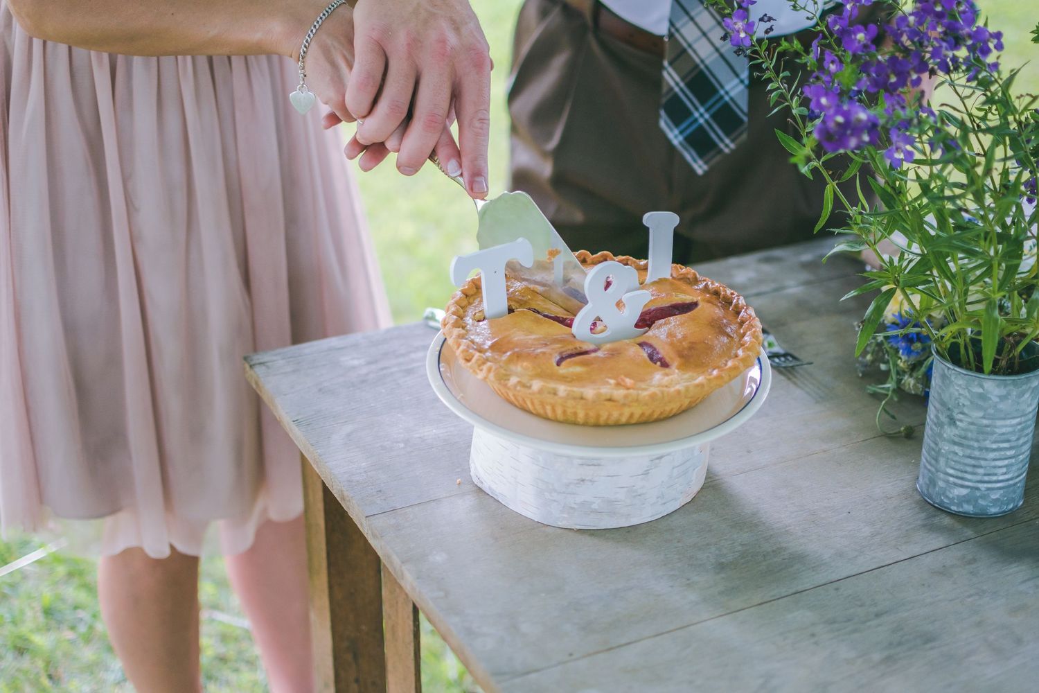 Cutting the cake, or in this case the pie! Bride and Groom guide one another as they cut a slice of pie to share at their outdoor reception.