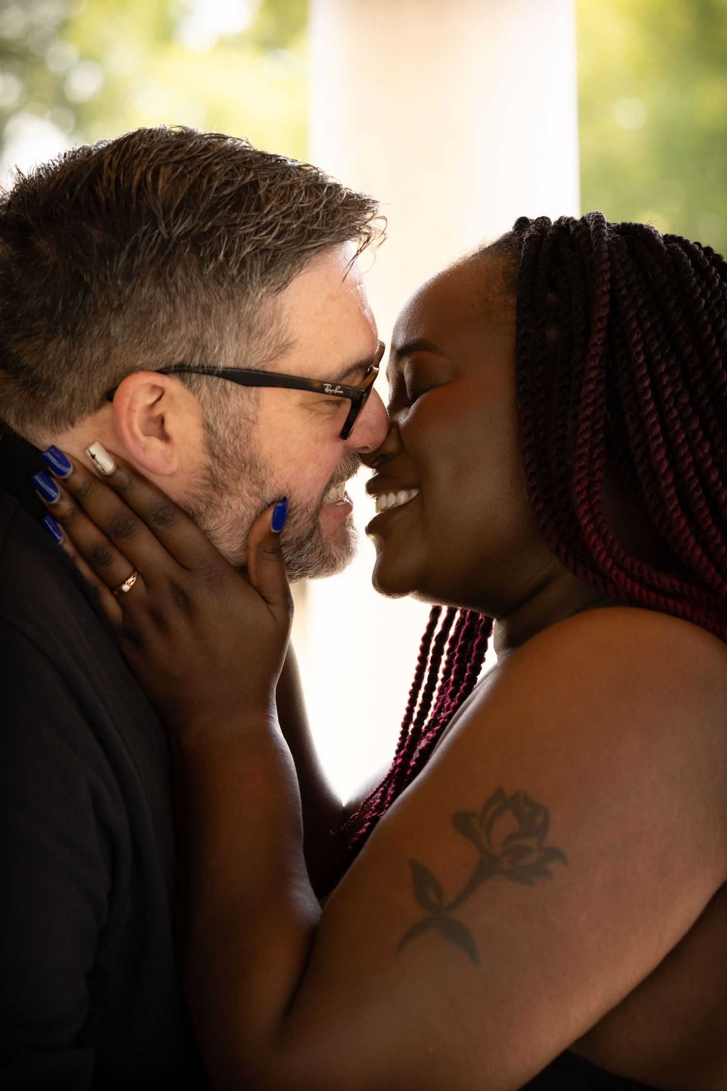 Interracial couple sharing a romantic moment, woman with braids and rose tattoo tenderly holding mans face as they lean in to kiss.