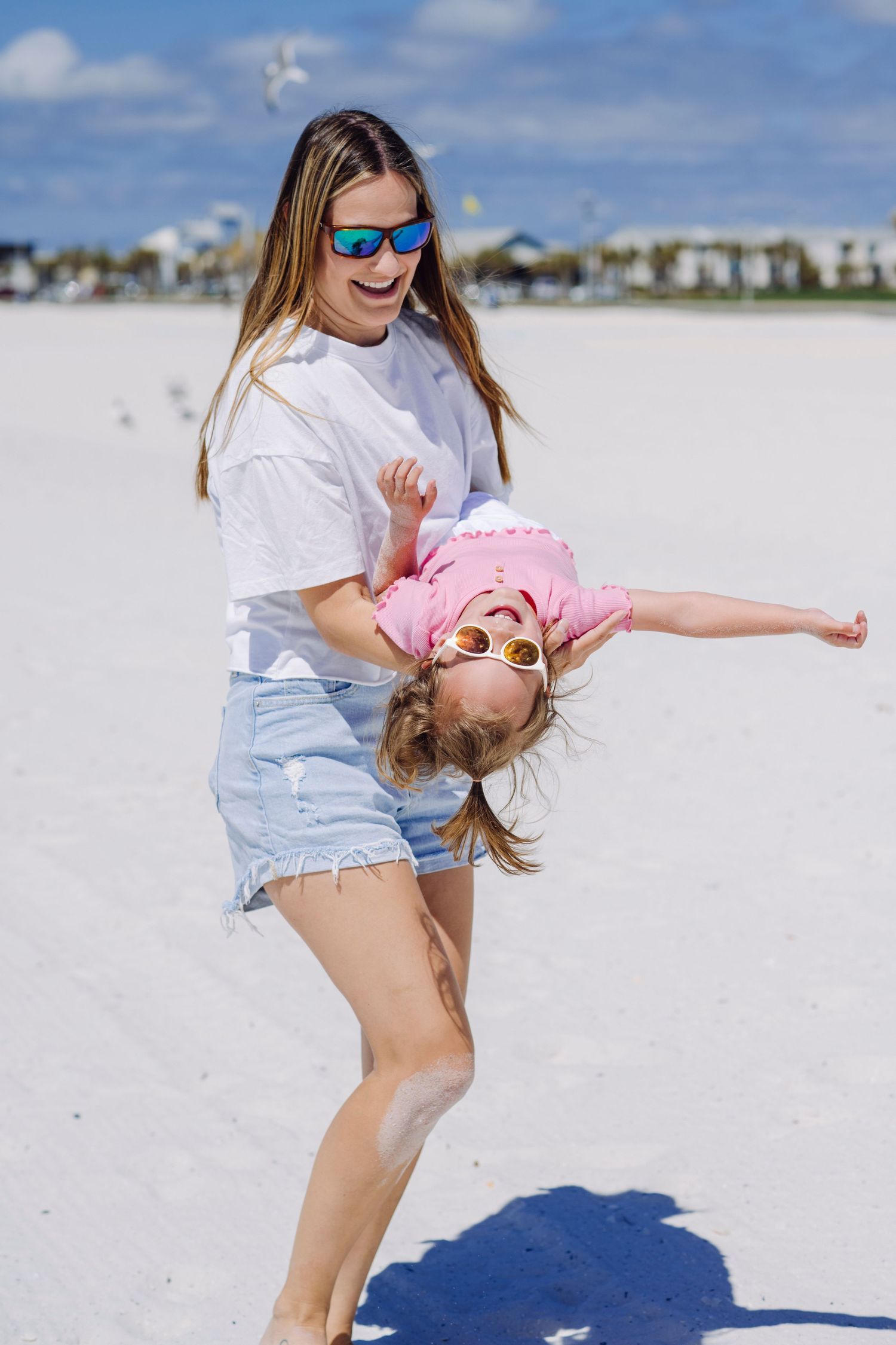 A playful scene on a white sandy beach with blue sky and buildings visible in the background.