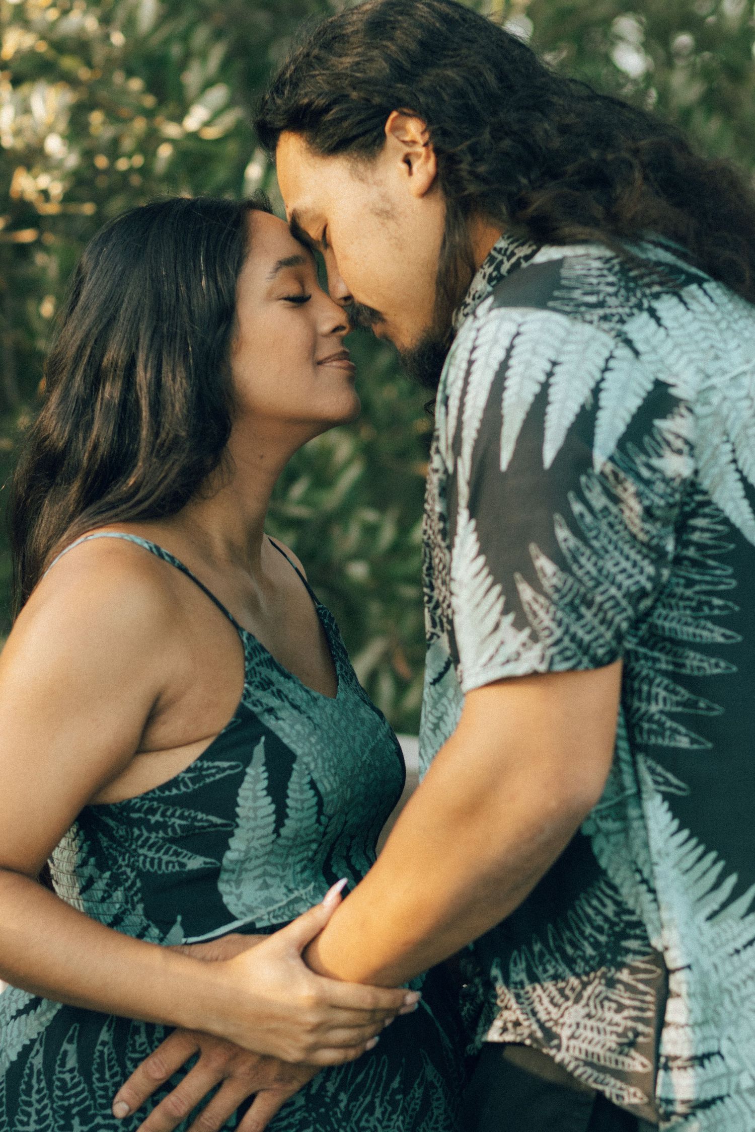 Couple embraces intimately outdoors against natural foliage background in romantic photo series.