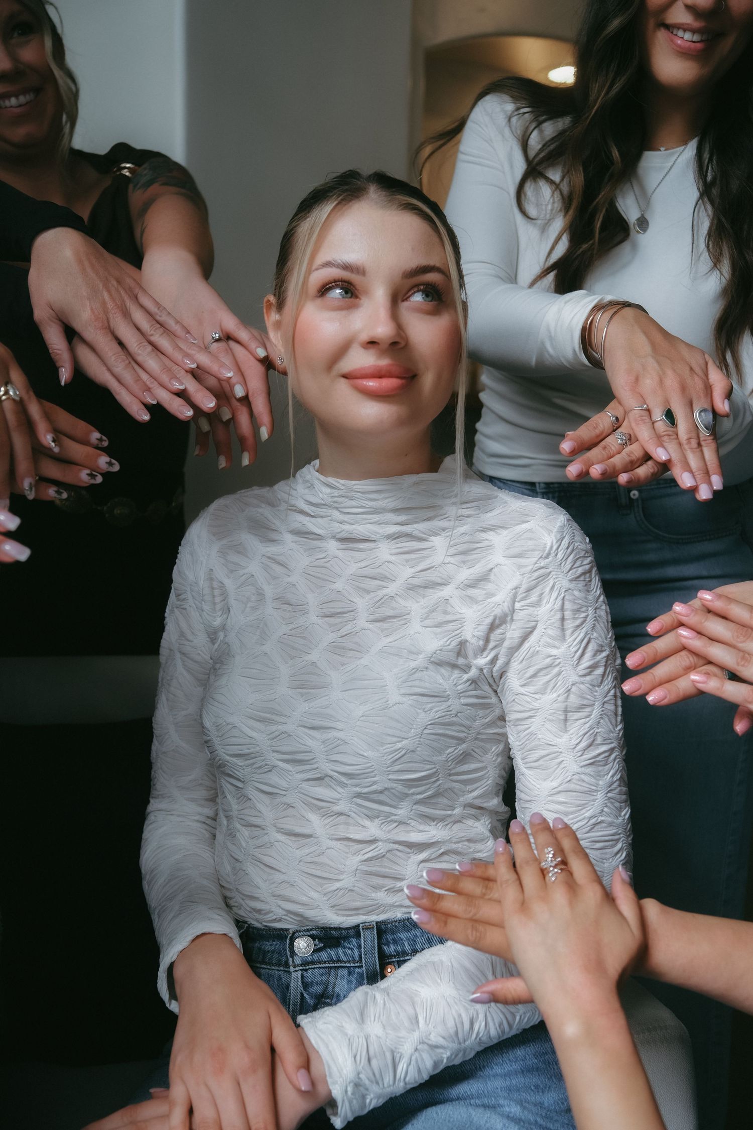 Young woman in white turtleneck seated while friends surround her showing off their manicured nails.